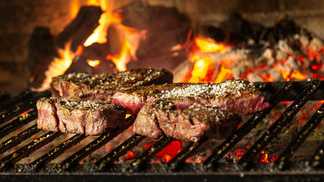 Steak sizzling on a bbq. Coal and firewood being used