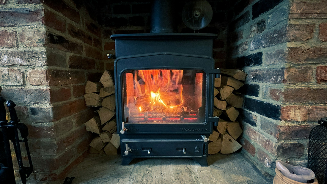 Log burner situated in a fireplace, burning away with a pile of logs next to it